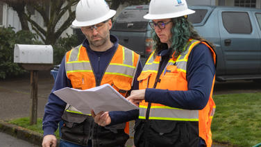 Two employees reviewing plans on site of a project.